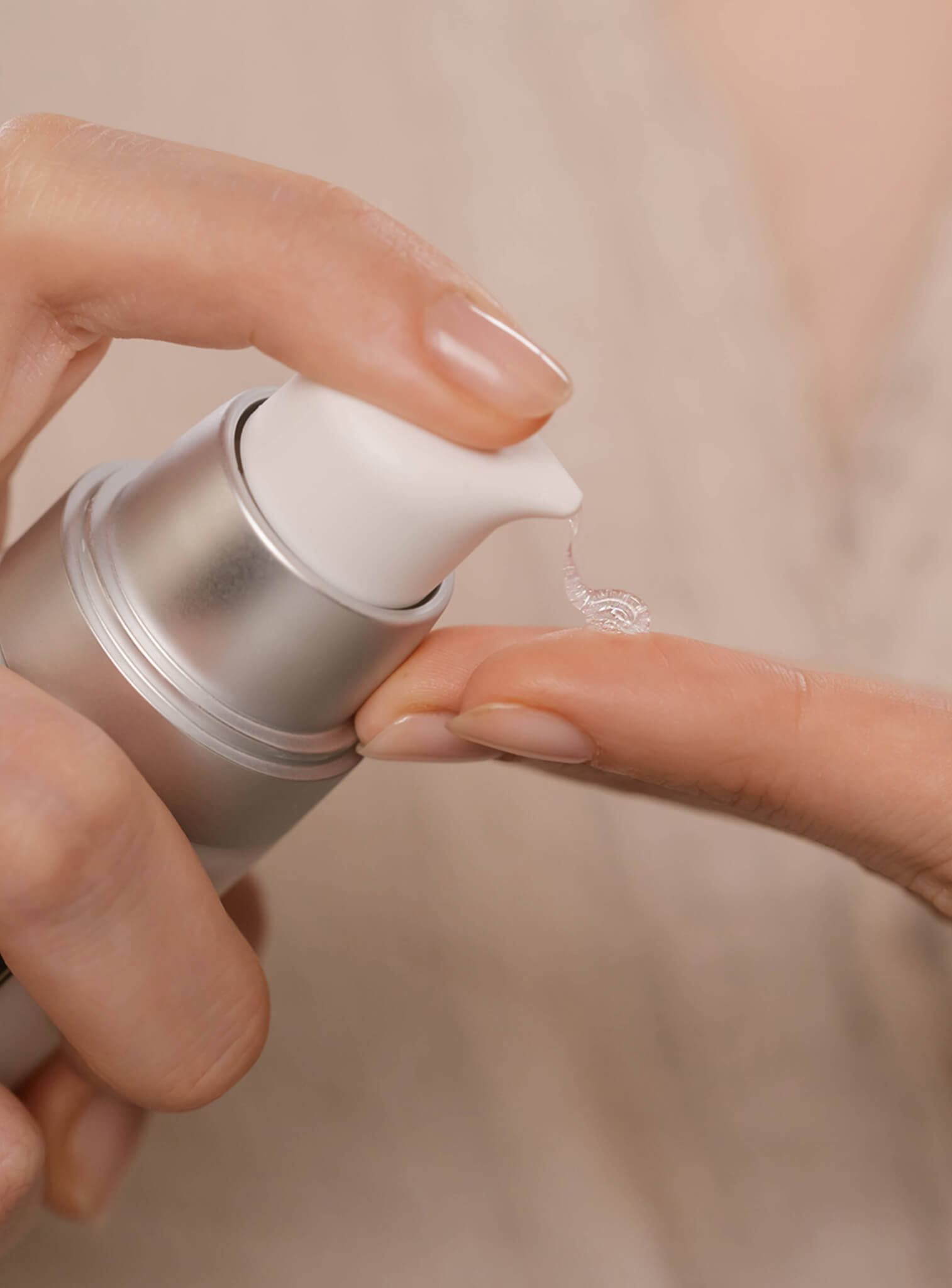 Hand holding a silver and white skincare product with a beige background