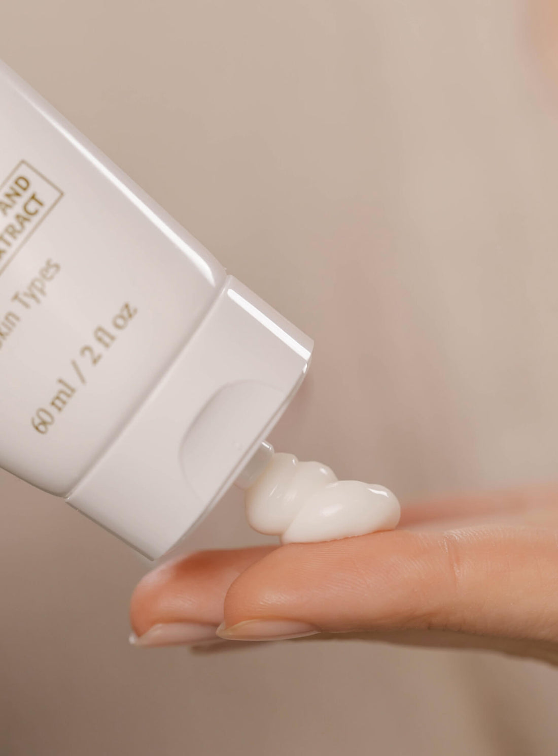 Hand holding a small white container of cream with a beige background