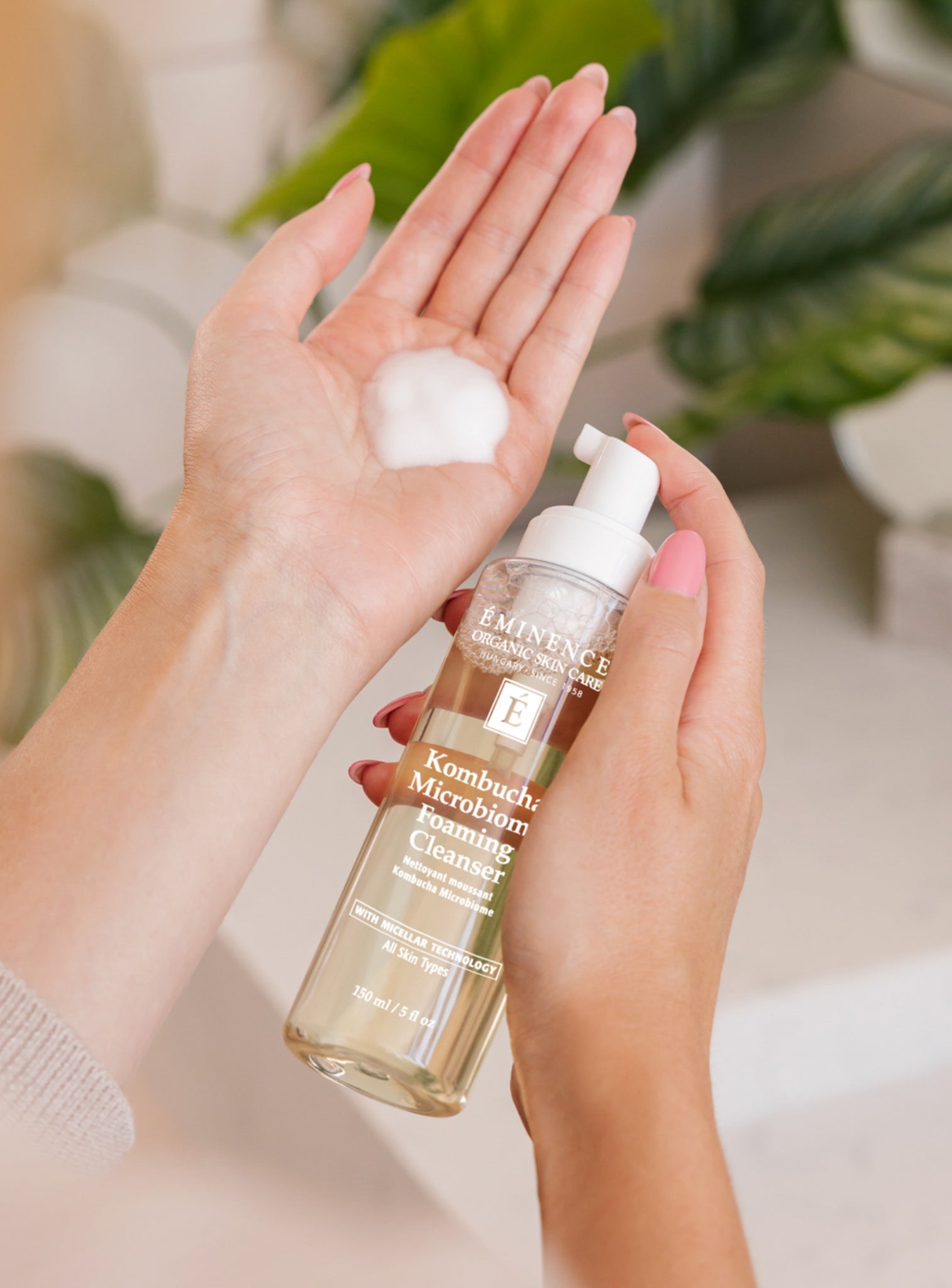 Person holding a bottle of Eminence Kombucha Microbiome Foaming Cleanser with a small amount on their palm.